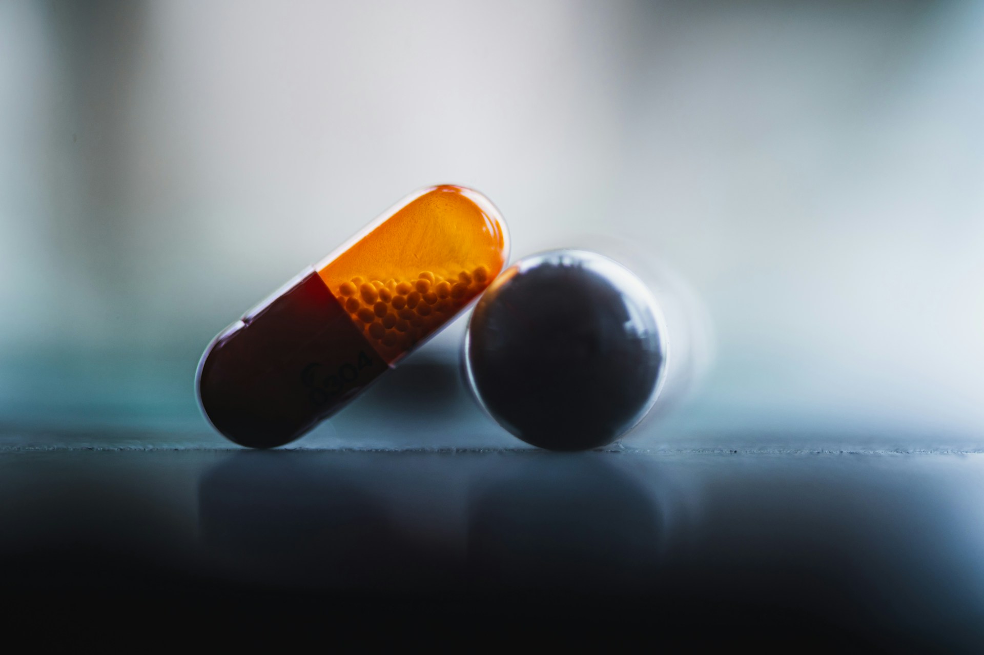 Macro photograph of a two-tone capsule filled with orange pellets, resting against a dark spherical tablet